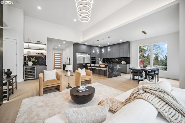 living area featuring beverage cooler, light wood finished floors, an inviting chandelier, recessed lighting, and bar