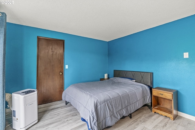 bedroom with a textured ceiling, baseboards, and wood finished floors