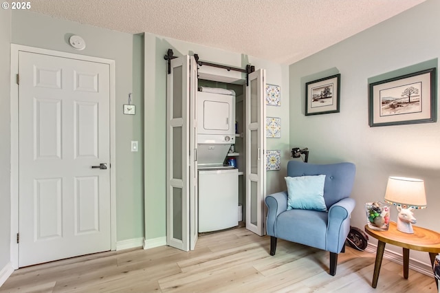 living area featuring stacked washer / dryer, light wood-style floors, baseboards, a barn door, and a textured ceiling