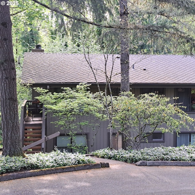 view of front facade with board and batten siding, stairway, a chimney, and a shingled roof