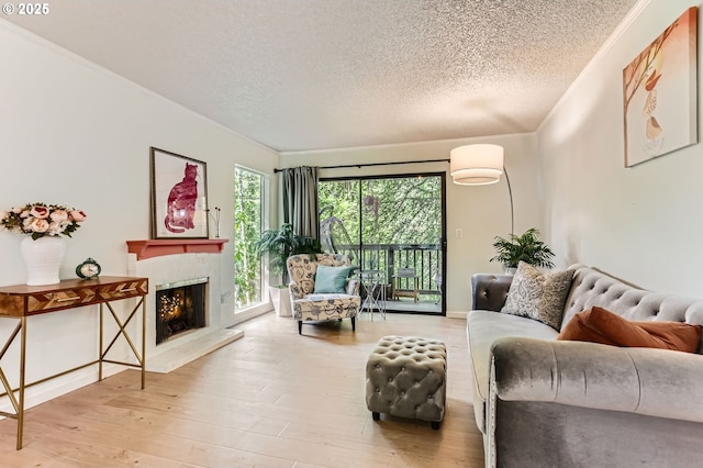 living area featuring crown molding, a warm lit fireplace, a textured ceiling, and wood finished floors