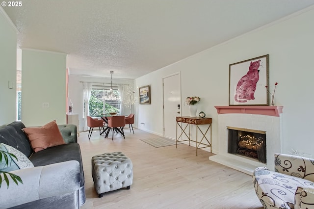 living area with crown molding, a fireplace with raised hearth, a textured ceiling, a chandelier, and wood finished floors