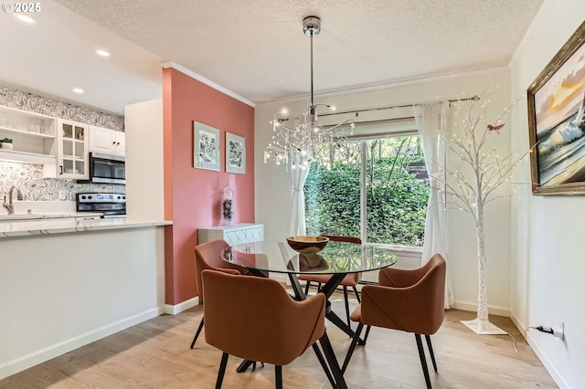 dining area with light wood finished floors, a textured ceiling, a chandelier, recessed lighting, and ornamental molding