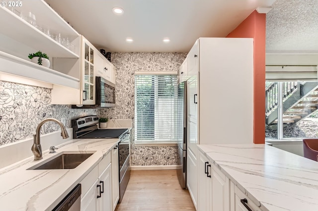 kitchen with light wood-type flooring, a sink, white cabinets, and stainless steel appliances