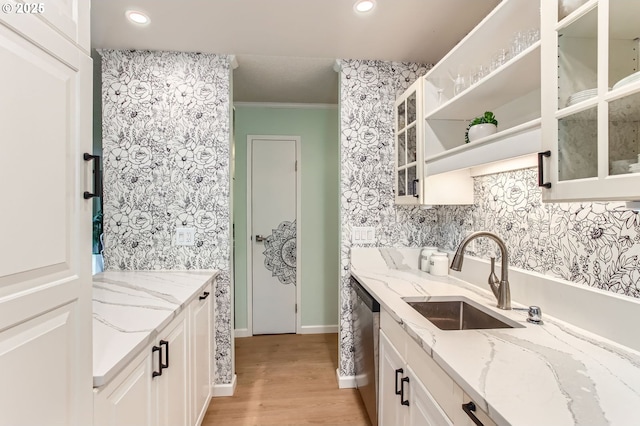 kitchen featuring stainless steel dishwasher, glass insert cabinets, light wood-style floors, light stone counters, and a sink