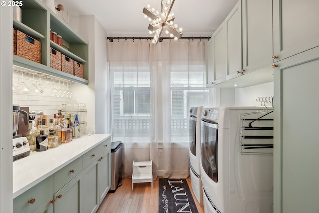 clothes washing area featuring cabinets, washing machine and clothes dryer, an inviting chandelier, and light hardwood / wood-style flooring