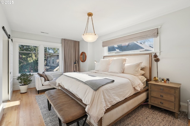 bedroom with a barn door and light wood-type flooring