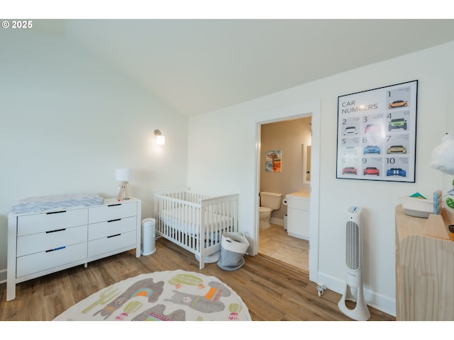 bedroom featuring vaulted ceiling, ensuite bathroom, light wood-style flooring, and baseboards