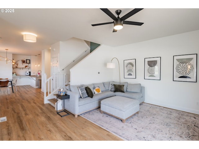 living room with visible vents, a ceiling fan, wood finished floors, baseboards, and stairs