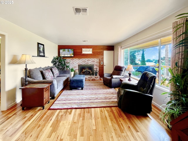 living area with a brick fireplace, baseboards, light wood finished floors, and visible vents