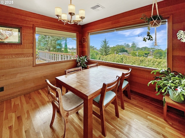 dining room with a notable chandelier, visible vents, light wood-style flooring, and wood walls