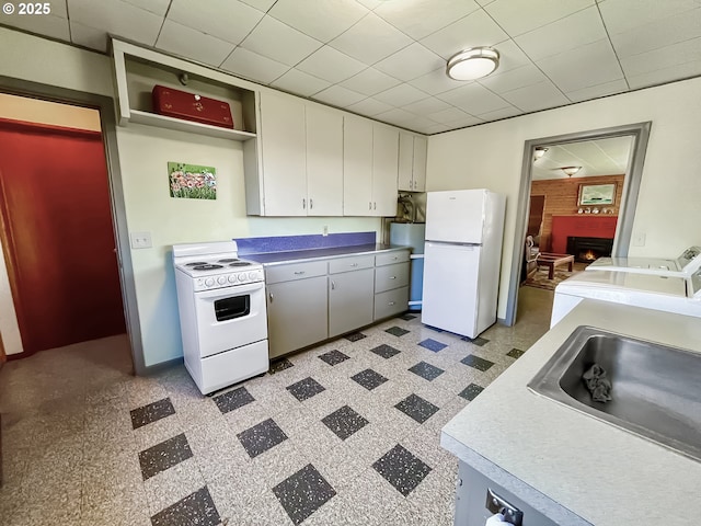 kitchen featuring open shelves, white appliances, baseboards, a sink, and a warm lit fireplace