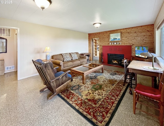 living room with a warm lit fireplace, wooden walls, baseboards, and visible vents