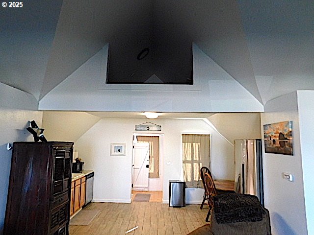 kitchen with stainless steel dishwasher, light wood-type flooring, and vaulted ceiling