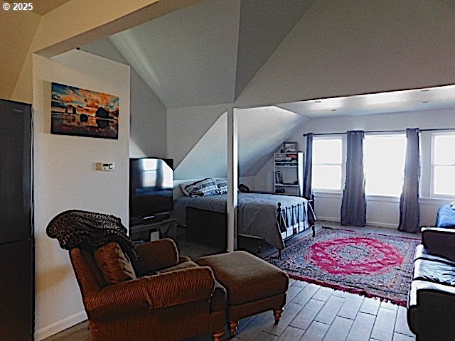 bedroom featuring black refrigerator, wood-type flooring, and vaulted ceiling