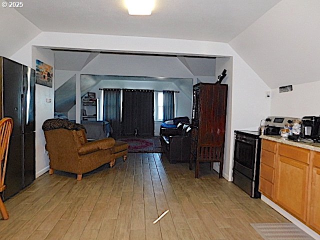 kitchen with light hardwood / wood-style flooring, black appliances, and vaulted ceiling