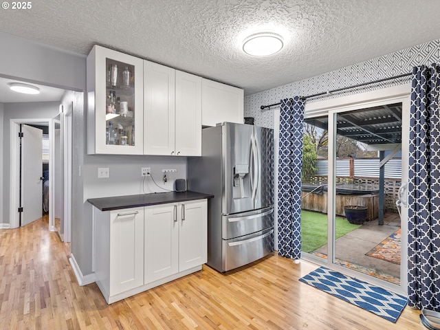 kitchen featuring dark countertops, white cabinetry, stainless steel fridge with ice dispenser, light wood finished floors, and glass insert cabinets