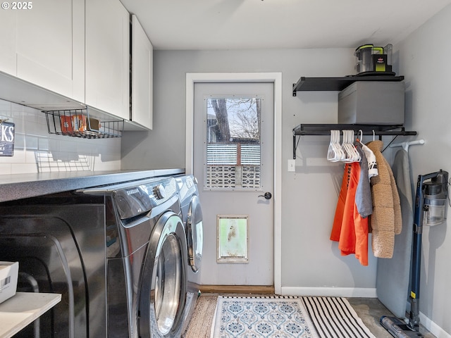 clothes washing area featuring washing machine and clothes dryer, cabinet space, and baseboards