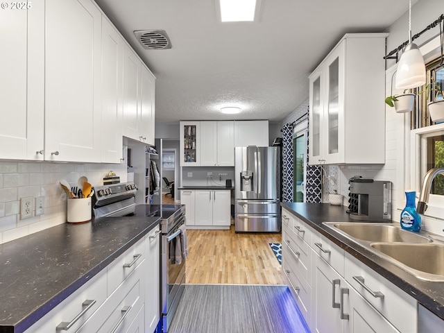 kitchen featuring visible vents, a sink, dark countertops, stainless steel appliances, and light wood finished floors