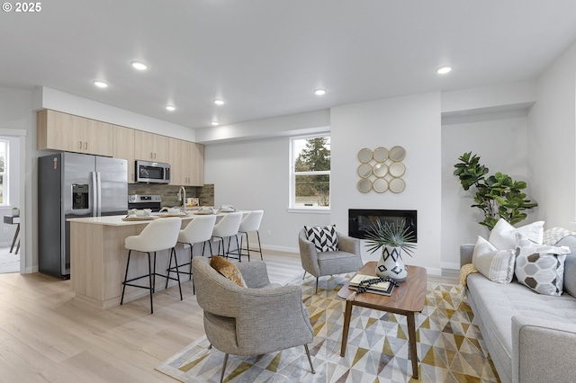 living room with recessed lighting, baseboards, light wood-style floors, and a glass covered fireplace