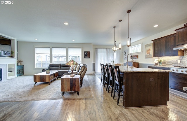 kitchen with light wood-type flooring, a center island with sink, open floor plan, dark brown cabinetry, and a breakfast bar area