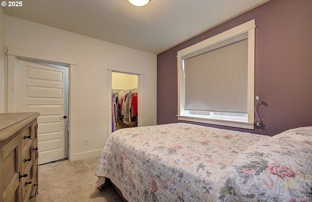 bedroom featuring a walk in closet, baseboards, light carpet, a closet, and a textured ceiling