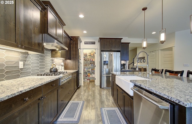 kitchen with under cabinet range hood, a sink, appliances with stainless steel finishes, light wood finished floors, and light stone countertops