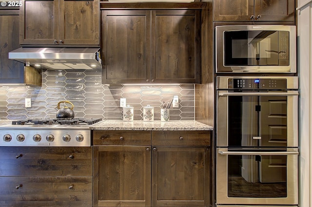 kitchen with under cabinet range hood, decorative backsplash, dark brown cabinets, and appliances with stainless steel finishes