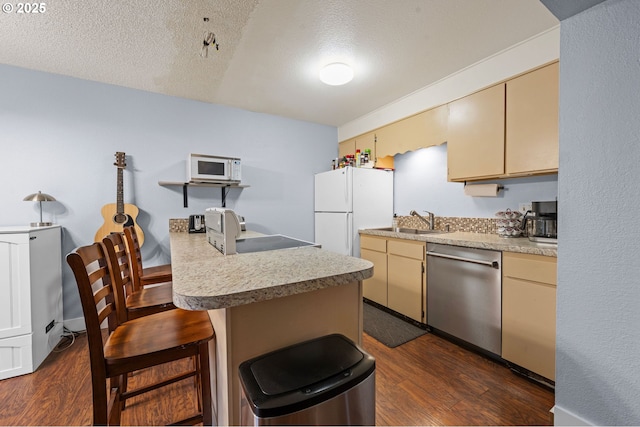 kitchen with cream cabinets, a peninsula, white appliances, a sink, and dark wood finished floors