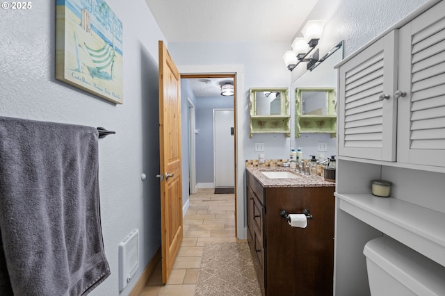 bathroom with baseboards, visible vents, toilet, a textured ceiling, and vanity