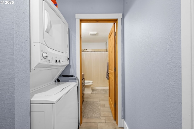 washroom with a textured wall, laundry area, and stacked washer / drying machine