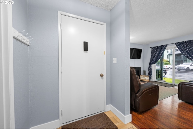 entryway with a textured ceiling, a textured wall, wood finished floors, and baseboards