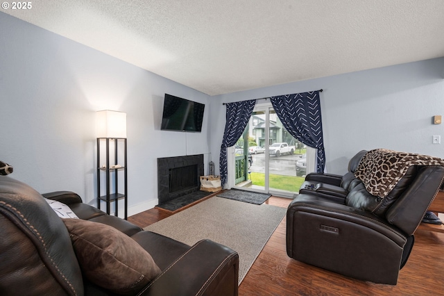 living area featuring a fireplace, a textured ceiling, baseboards, and wood finished floors