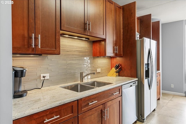 kitchen with tasteful backsplash, baseboards, appliances with stainless steel finishes, light stone counters, and a sink