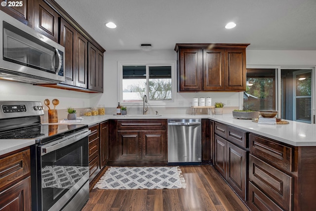 kitchen featuring a sink, dark wood-style floors, appliances with stainless steel finishes, a peninsula, and light countertops