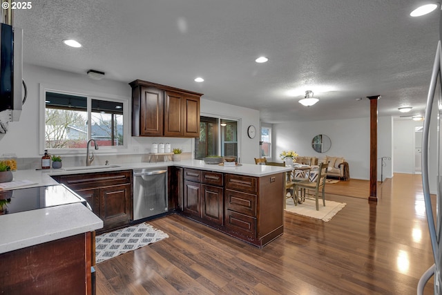 kitchen with a sink, dark wood-style floors, stainless steel appliances, a peninsula, and light countertops