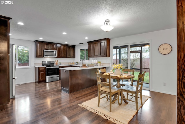 kitchen featuring dark brown cabinetry, dark wood finished floors, light countertops, appliances with stainless steel finishes, and a peninsula