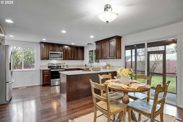 kitchen with dark brown cabinets, dark wood finished floors, light countertops, a peninsula, and stainless steel appliances