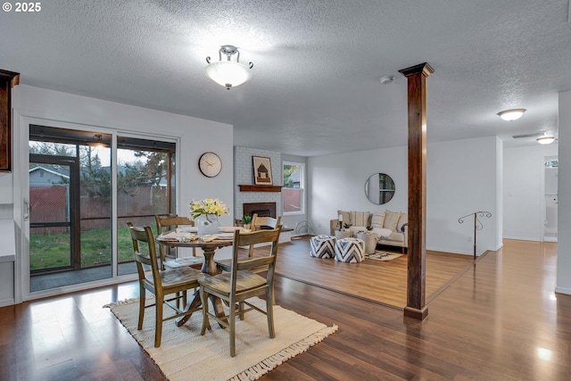 dining area with a brick fireplace, a textured ceiling, baseboards, and wood finished floors