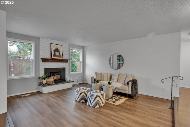 living area featuring visible vents, a brick fireplace, baseboards, wood finished floors, and a textured ceiling