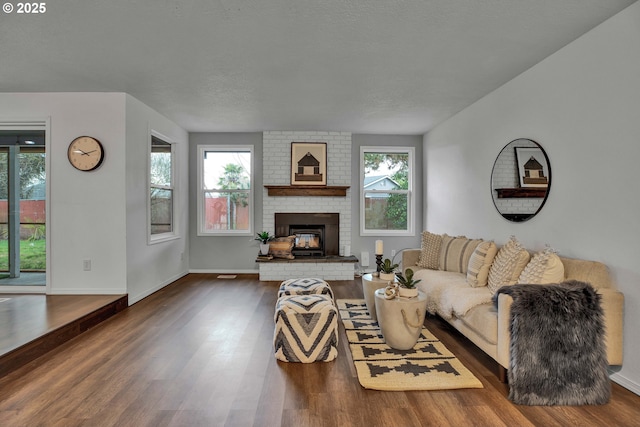 living room featuring baseboards, plenty of natural light, a brick fireplace, and dark wood finished floors