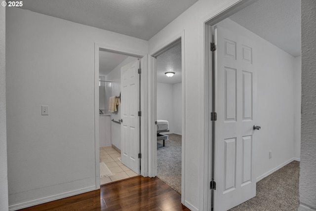 corridor with carpet floors, a textured ceiling, baseboards, and wood finished floors