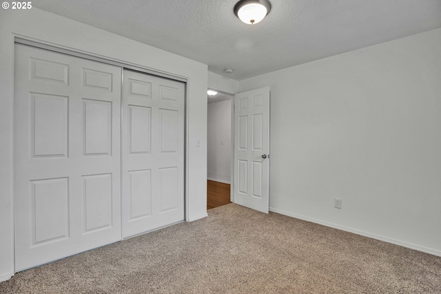 unfurnished bedroom featuring a closet, carpet floors, a textured ceiling, and baseboards