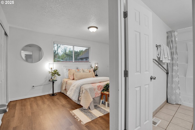 bedroom featuring visible vents, a textured ceiling, light wood-type flooring, and baseboards