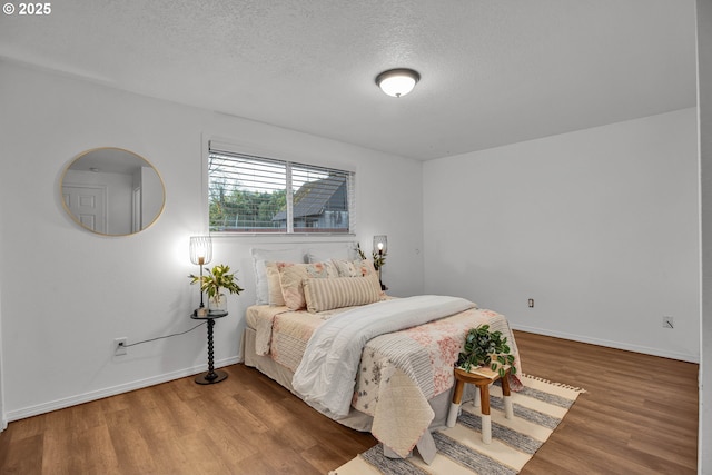 bedroom featuring a textured ceiling, baseboards, and wood finished floors