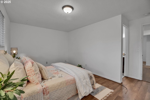 bedroom with wood finished floors, baseboards, and a textured ceiling