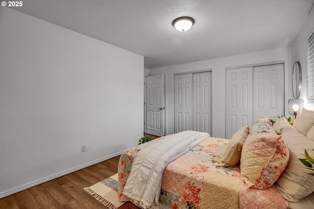 bedroom featuring a textured ceiling, baseboards, multiple closets, and wood finished floors