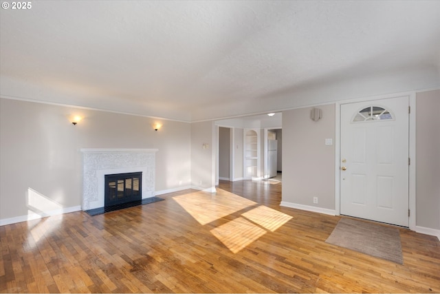 unfurnished living room featuring built in shelves, light hardwood / wood-style flooring, ornamental molding, and a textured ceiling