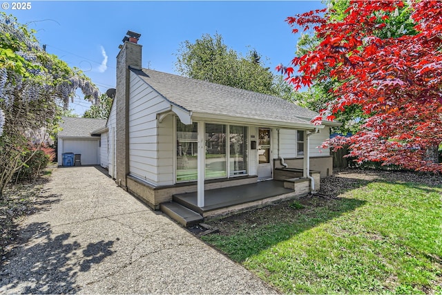 view of front facade featuring a shingled roof, driveway, a front yard, and a chimney