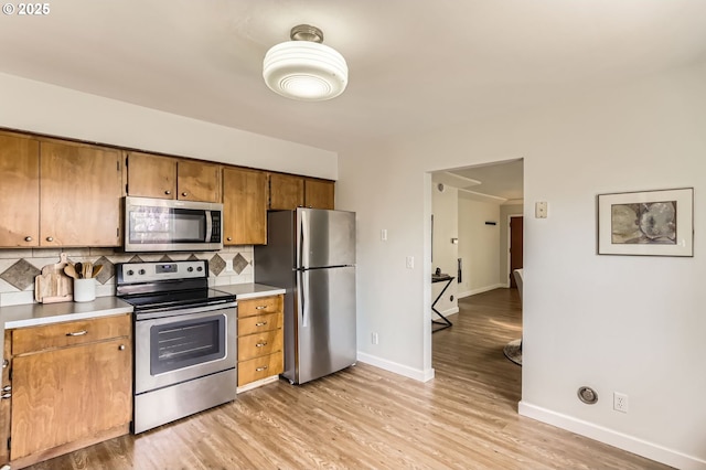 kitchen featuring baseboards, brown cabinets, tasteful backsplash, light wood finished floors, and appliances with stainless steel finishes